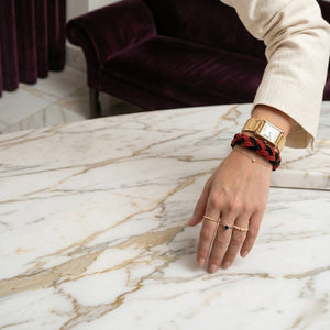 Hand wearing a red and black braided bracelet with text 'Define High-quality natural suede bracelet Hand-braided, sporty, and casual Unisex design, perfect for everyday wear